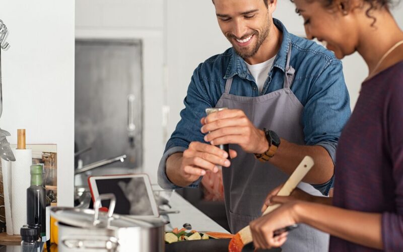 Couple cooking together, man sprinkling seasoning