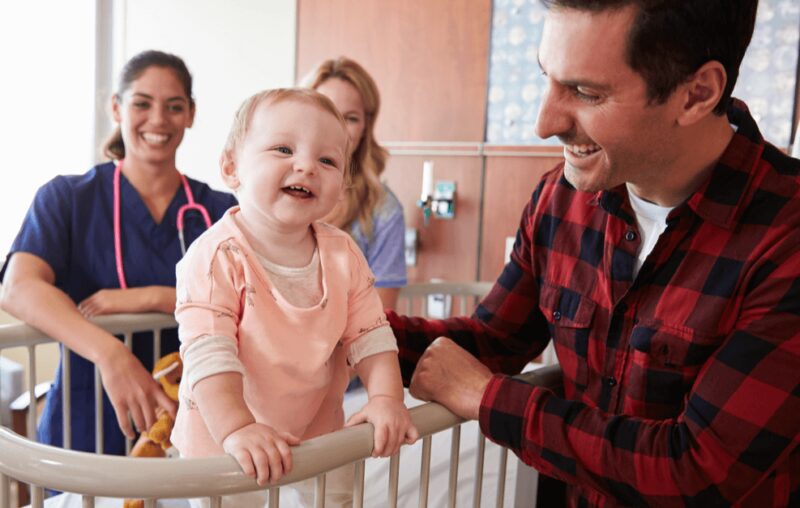 Smiling baby standing in crib with family