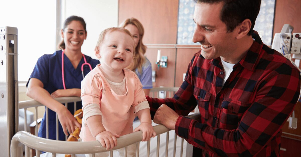 Smiling baby standing in crib with family