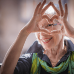 Elderly woman smiling while looking through fingers forming a heart